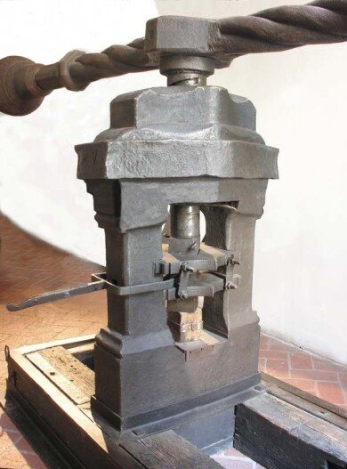 A historic screw press, with its weighted spinning bar visible above the striking chamber